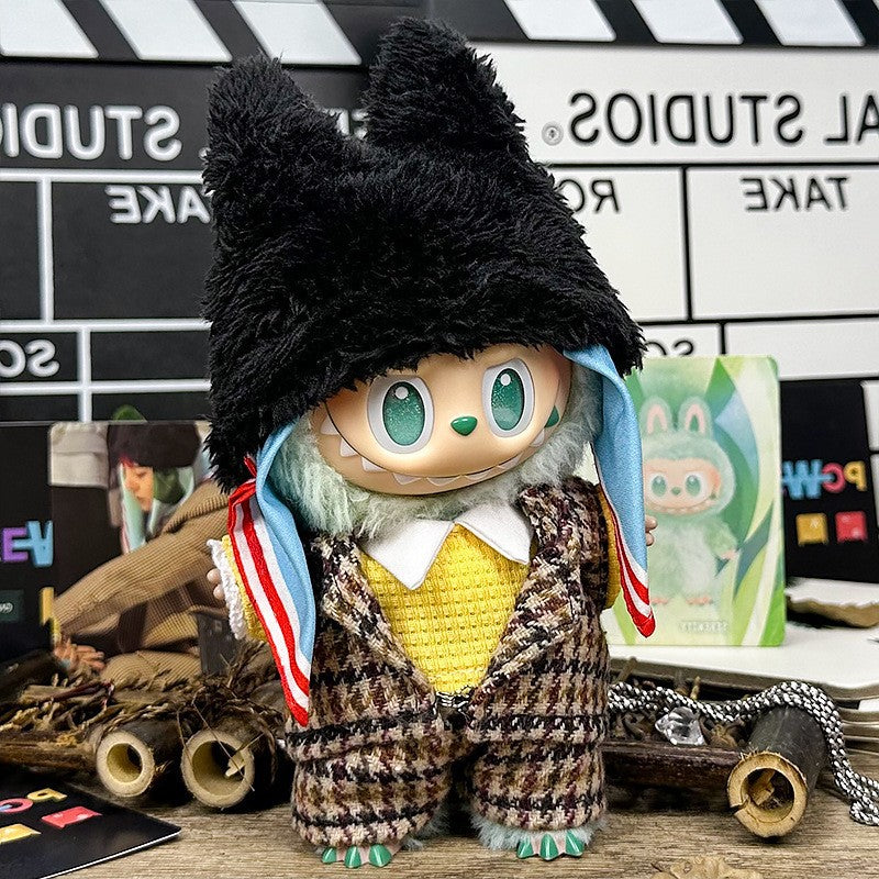 A ZoDoll Labubu Doll in a brown tweed plaid suit set with a black fluffy bear hat stands on a craft-filled table with a movie clapperboard backdrop, its big green eyes watching over the creative chaos.