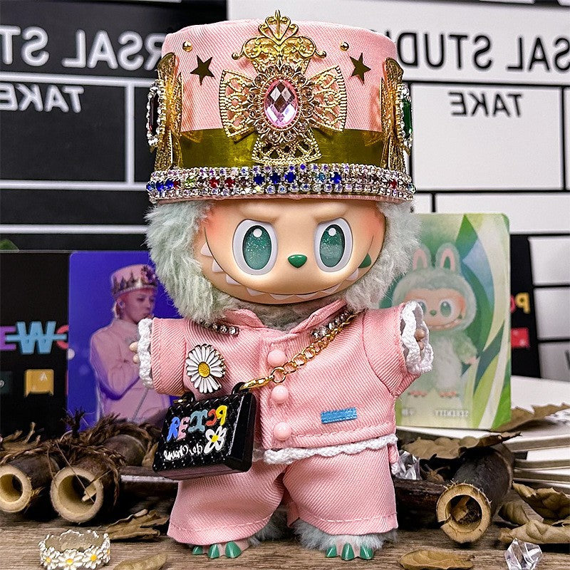 The ZoDoll Labubu Pink Royal Twill Suit Set, featuring a crown hat and mini bag, stands on a table adorned with decorative items and background photos.