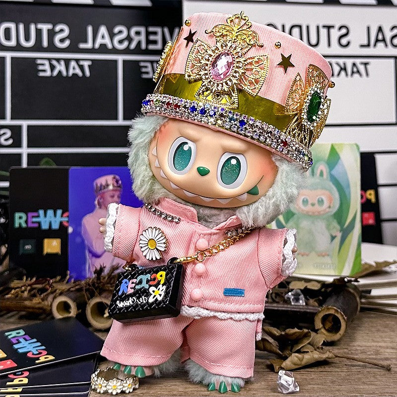 The ZoDoll Labubu Pink Royal Twill Suit Set features a plush doll with large eyes, a jeweled crown hat, daisy-detailed pink suit, and a mini bag, displayed in front of trading cards and decor.