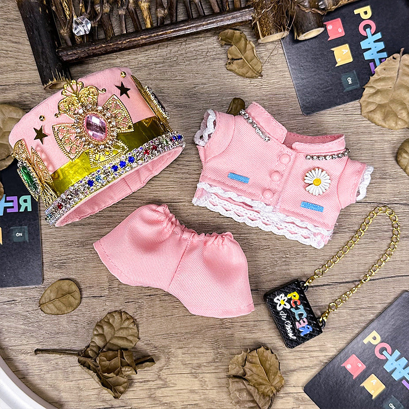 The ZoDoll Labubu Pink Royal Twill Suit Set includes a skirt, jacket, crown hat, and mini bag—an elegant designer doll outfit. Displayed on a wooden surface with leaves and cards for added charm.