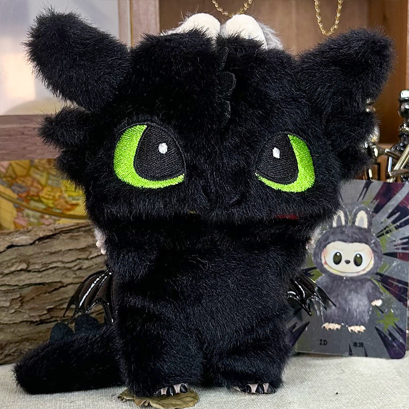 The ZoDoll Labubu Night Fury Dragon Black Plush, featuring large green eyes and a full-body costume outfit, stands before a small illustrated card, capturing the playful charm of a beloved black dragon.