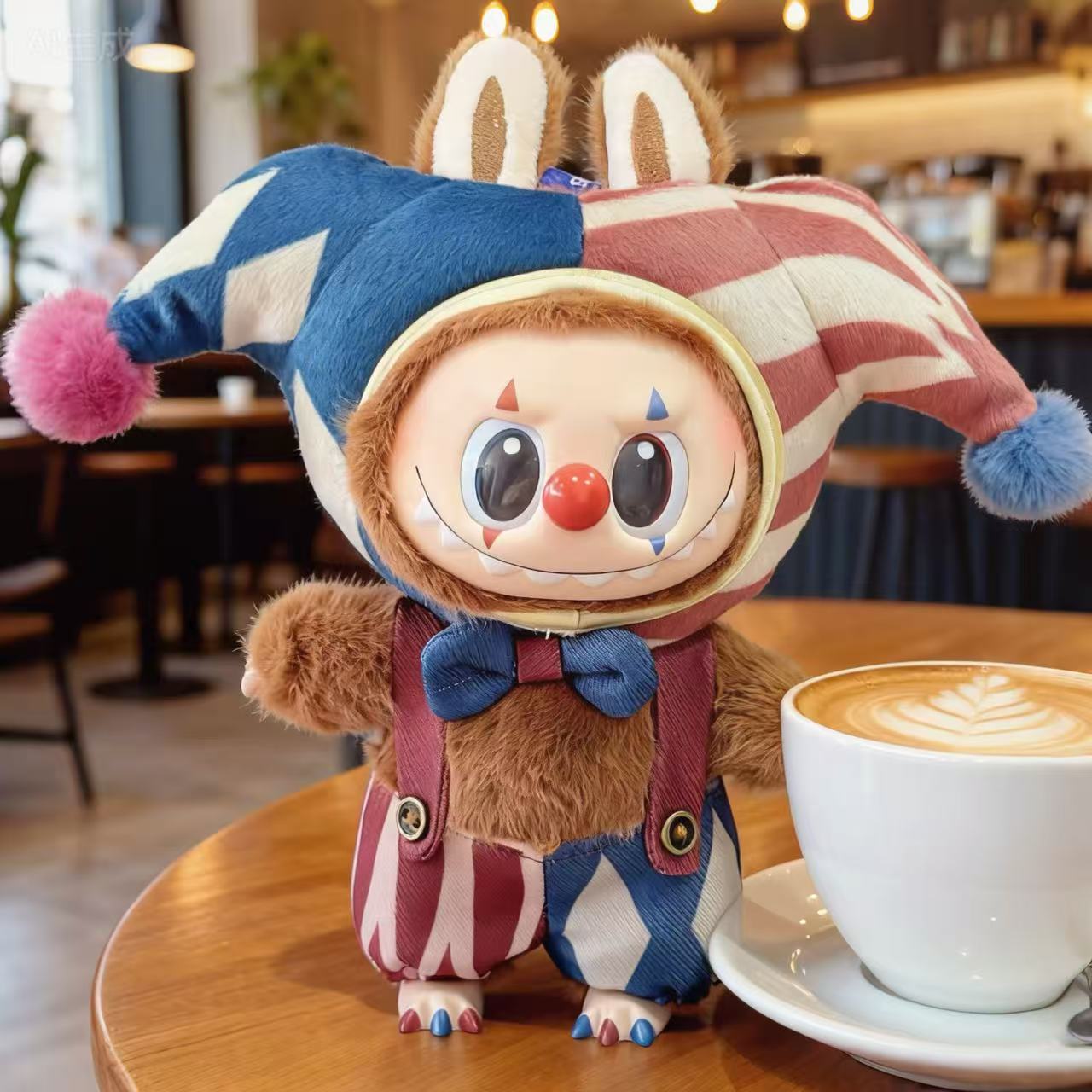 A ZoDoll Labubu Jester Clown Doll in a blue red harlequin circus outfit stands on a wooden table by a latte art cup, delighting Pop Mart fans in a cozy café setting.