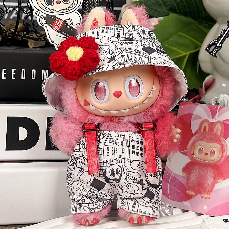 The ZoDoll Labubu Graffiti Print Overalls Set features a pink plush toy with large eyes, hooded cap, red suspenders, and a red flower accessory, displayed on a table with decorative items in the background.