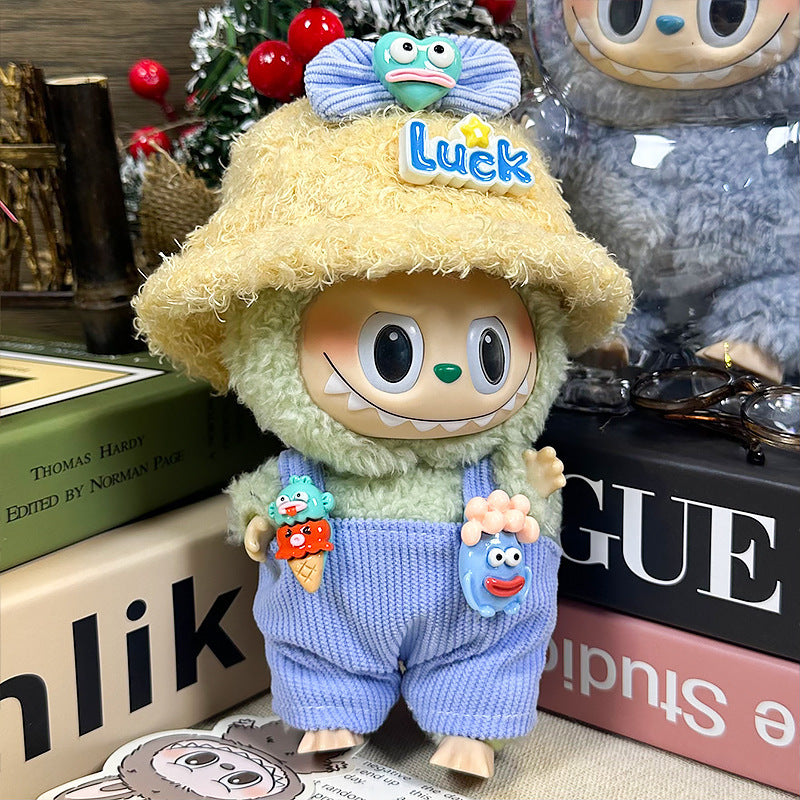 The ZoDoll Labubu Doll Lucky Bucket Hat and Corduroy Overalls Outfit Set features a plush doll with large eyes, a "Luck" bucket hat, green fuzzy top, and blue corduroy overalls, displayed among books and holiday décor.
