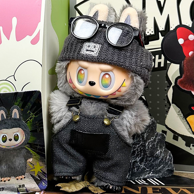The ZoDoll Labubu Doll wears a gray fuzzy coat, dark denim overalls, and a knit beanie with glasses, standing among colorful boxes and a matching character card.