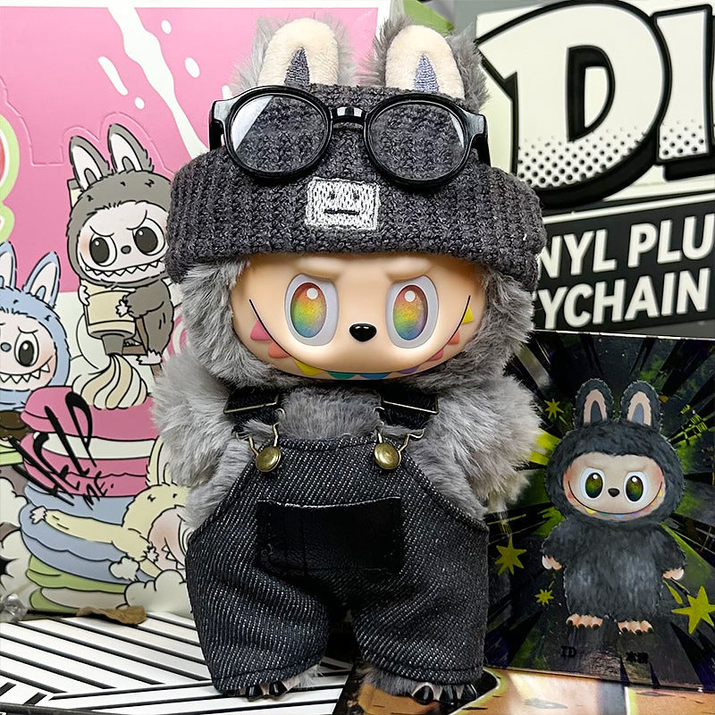 The ZoDoll Labubu Doll wears a gray fuzzy coat, dark denim overalls, and a knit beanie from the 3-piece set, posing with rainbow eyes and glasses against colorful cartoon-themed backgrounds.