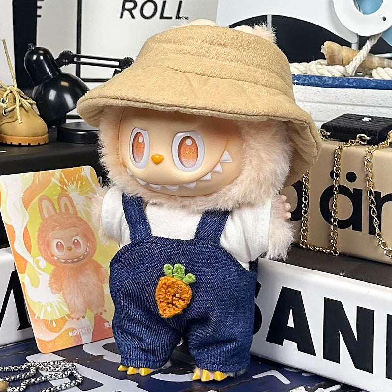 The ZoDoll Labubu Denim Overalls Set with Bucket Hat and Crochet Carrot Patch plush toy stands on a cluttered desk among various items, next to a card depicting a similar character in Labubu doll clothes.