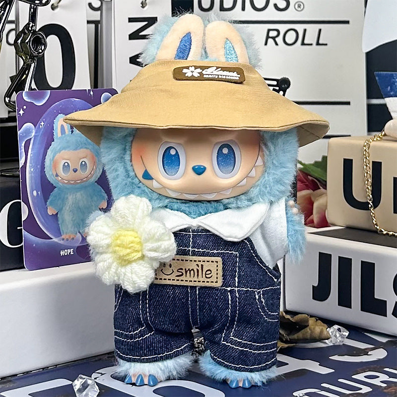 A ZoDoll Labubu plush wears the Denim Overalls and Wide-Brim Hat Outfit Set with Smile Patch, holding a white flower. A character card stands nearby among decorative items.