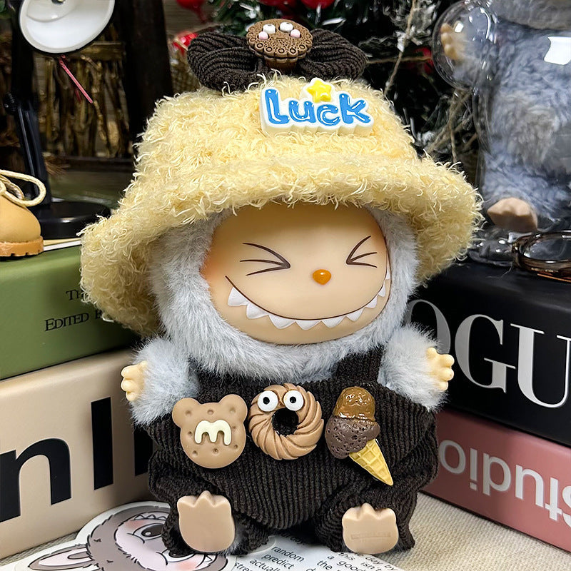 A ZoDoll Labubu Doll in a gray fuzzy hoodie, corduroy overalls, and a yellow "Luck" bucket hat sits on a table among books and other items.