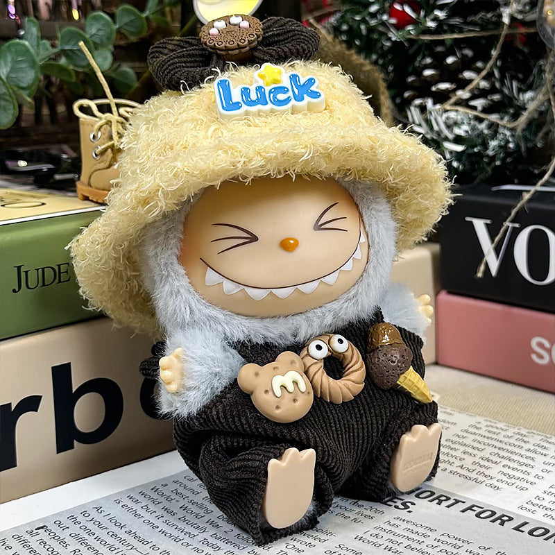 A smiling ZoDoll Labubu Doll in a gray fuzzy hoodie, corduroy overalls, and a Luck bucket hat from the "Labubu Doll Gray Fuzzy Hoodie and Corduroy Overalls with Luck Bucket Hat Set" sits among books and plants.