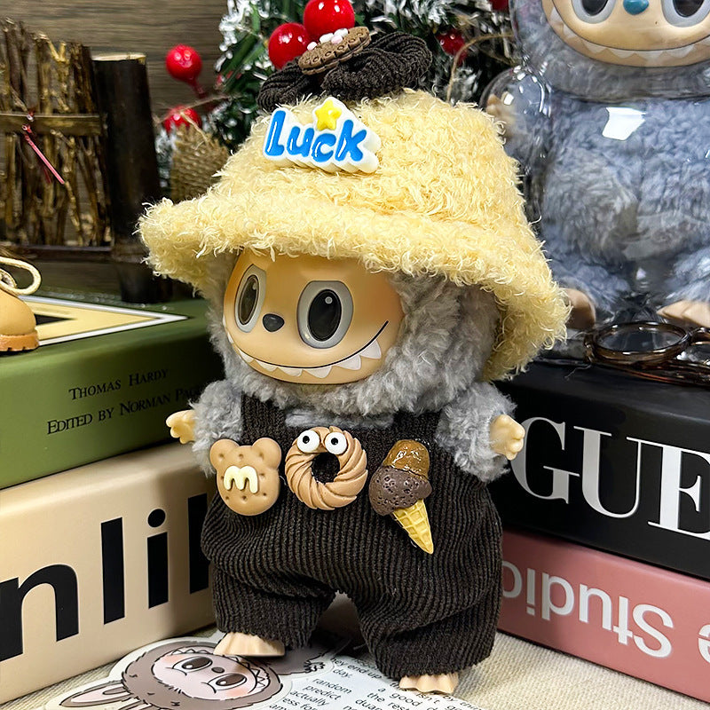 A ZoDoll Labubu Doll in a gray fuzzy hoodie, corduroy overalls, and a yellow Luck bucket hat stands on books, adorned with dessert pins; another Pop Mart Labubu figure appears in the background.