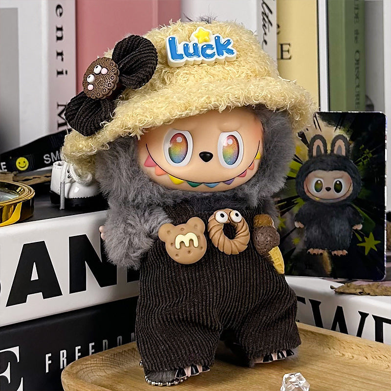 The ZoDoll Labubu Doll wears a gray fuzzy hoodie, corduroy overalls with bear faces, and a yellow "Luck" bucket hat, featuring rainbow eyes and a wide grin as it stands on a cluttered surface.