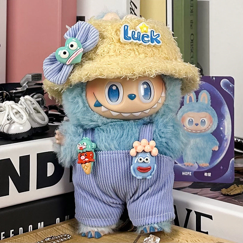 The ZoDoll Labubu Doll Lucky Bucket Hat and Corduroy Overalls Outfit Set features a plush toy with blue fur, big eyes, and a wide grin, wearing a "Luck" straw hat, corduroy overalls, and pins amid books and accessories.