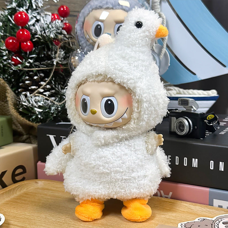 A ZoDoll Labubu White Fluffy Bird Kigurumi Doll, made from soft bouclé loop fabric and featuring orange feet, stands smiling on a wooden surface surrounded by decorative items and books.