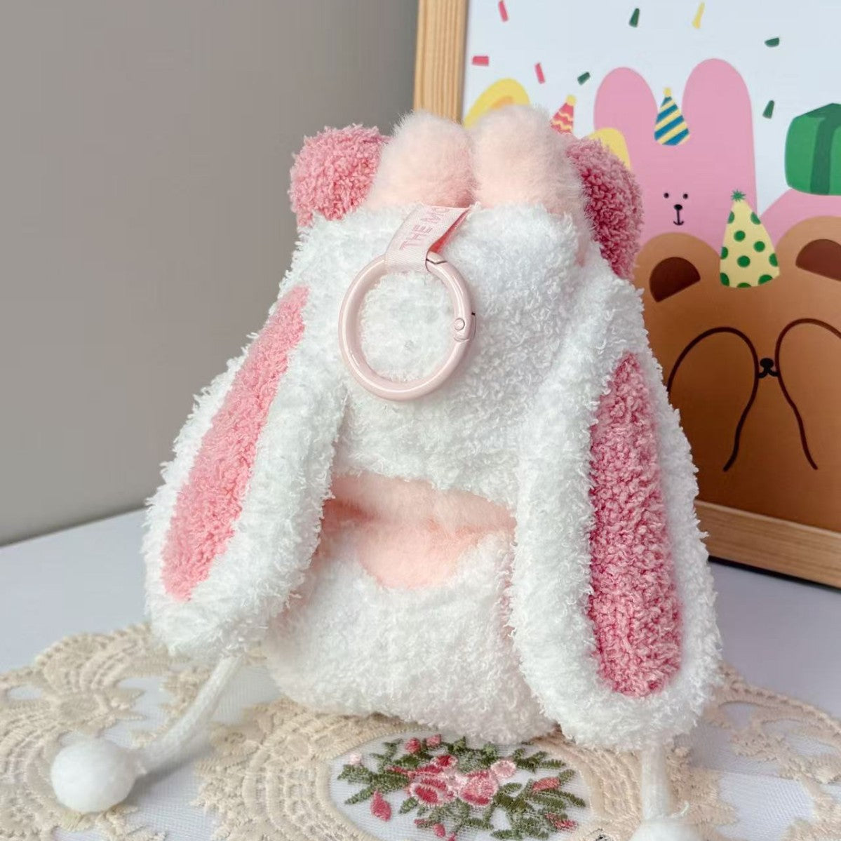 The ZoDoll Labubu Pink White Fluffy Bunny Onesie Plush Doll Costume—a small, fluffy backpack with bunny ears and pink accents—sits by a lace cloth, perfect for your Pop Mart Labubu plush or as a cute onesie costume accessory.