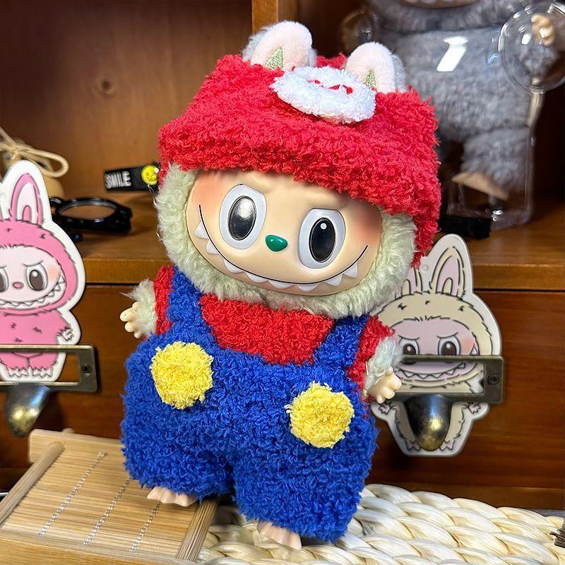 A ZoDoll Labubu Fluffy Plumber Costume Set plush, featuring a wide grin and dressed in a red cap and blue overalls, stands before wooden shelves decorated with bunny-themed items.