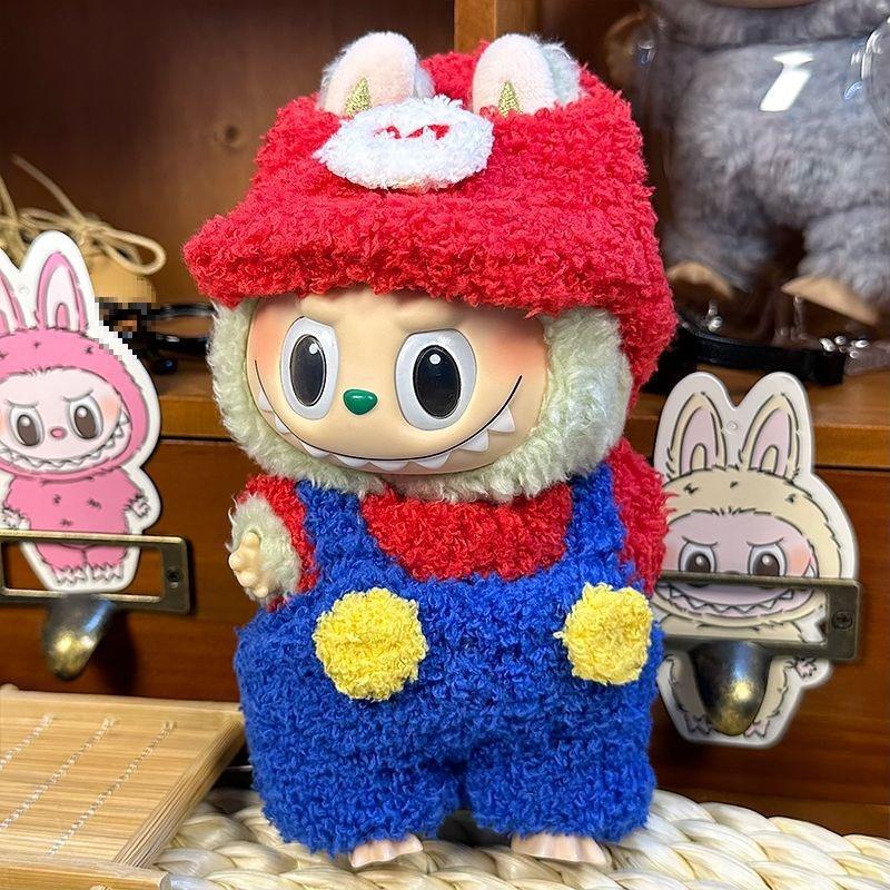 A ZoDoll Labubu Fluffy Plumber Costume Set plush, featuring a red cap and blue overalls, stands before bunny-themed decorations on a wooden shelf.