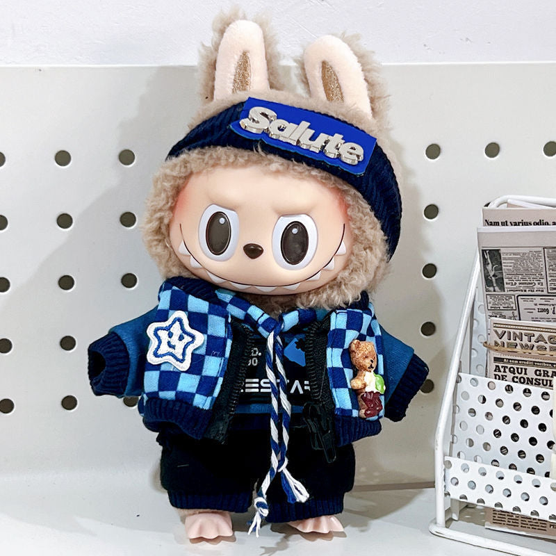 The ZoDoll Labubu Doll wears a navy streetwear set with a Salute beanie and checkerboard scarf, standing by a white rack with rolled newspapers.