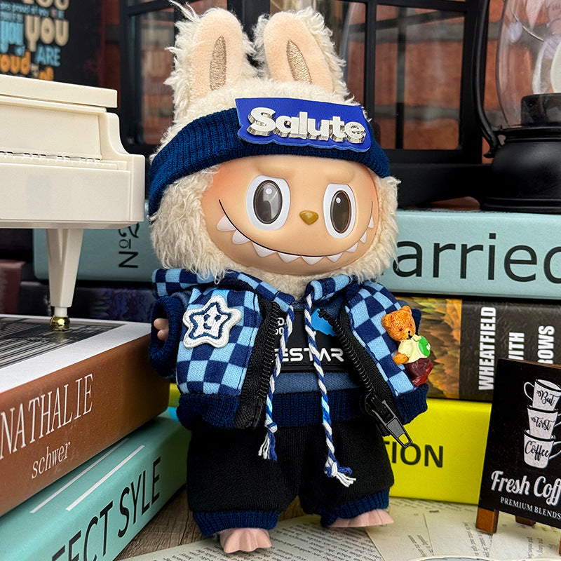 A ZoDoll Labubu Doll in a Navy Streetwear Set with Salute Beanie and Checkerboard Scarf stands on books next to a small teddy bear and a miniature white piano.