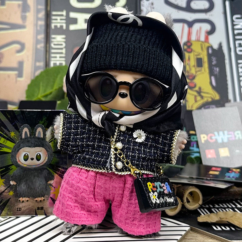 The ZoDoll Labubu plush wears the Designer Tweed Jacket and Hot Pink Pants Luxury Doll Outfit Set, complete with a black beanie, sunglasses, scarf, and purse, posing stylishly among colorful cards and objects.