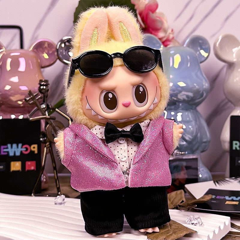 A ZoDoll Labubu Doll in a pink sequin blazer tuxedo outfit with black bow tie stands on a table decorated with colorful bear-shaped accents and playful Pop Mart Labubu accessories in the background.