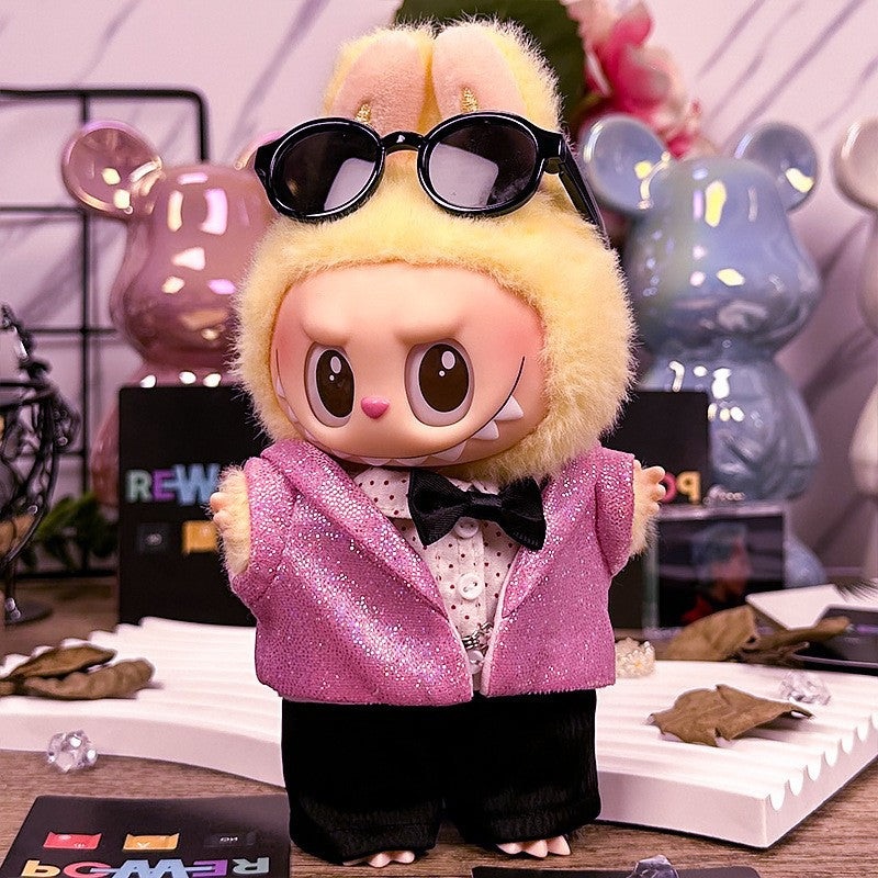 A ZoDoll Labubu Doll in a pink sequin blazer tuxedo outfit with a black bow tie and yellow bunny hoodie stands on a table, surrounded by decorative items and bear-shaped figures in the background.