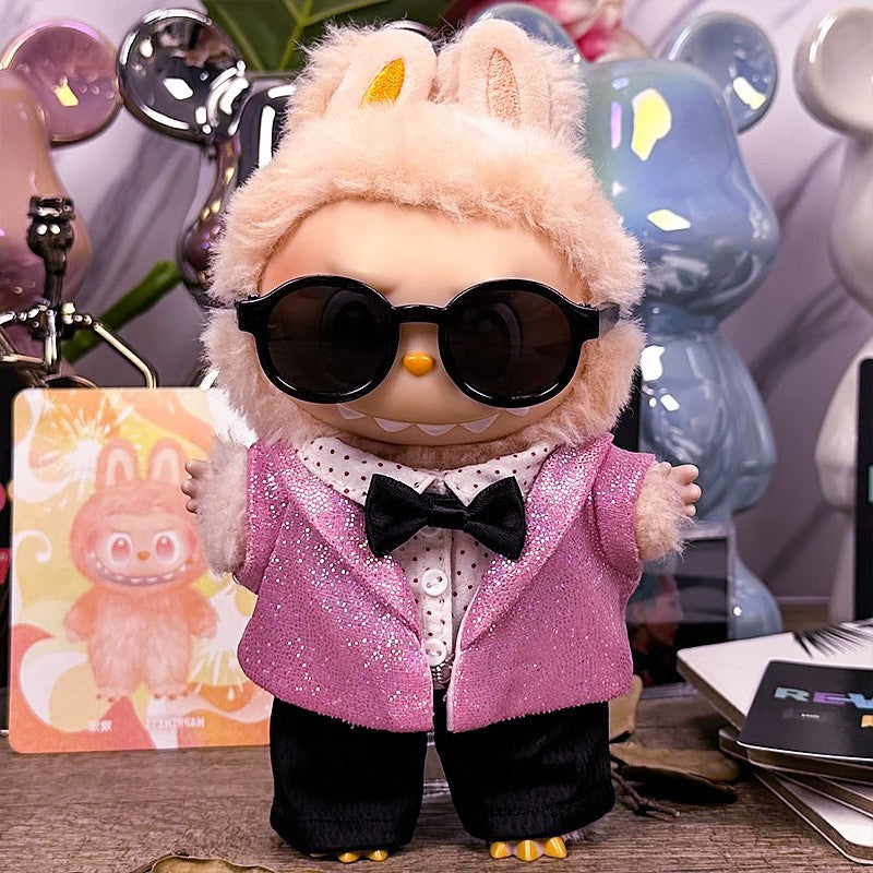 A ZoDoll Labubu Doll in a Pink Sequin Blazer Tuxedo Outfit with Black Bow Tie and sunglasses stands on a table, with Pop Mart Labubu accessories and bear-shaped figures visible in the background.