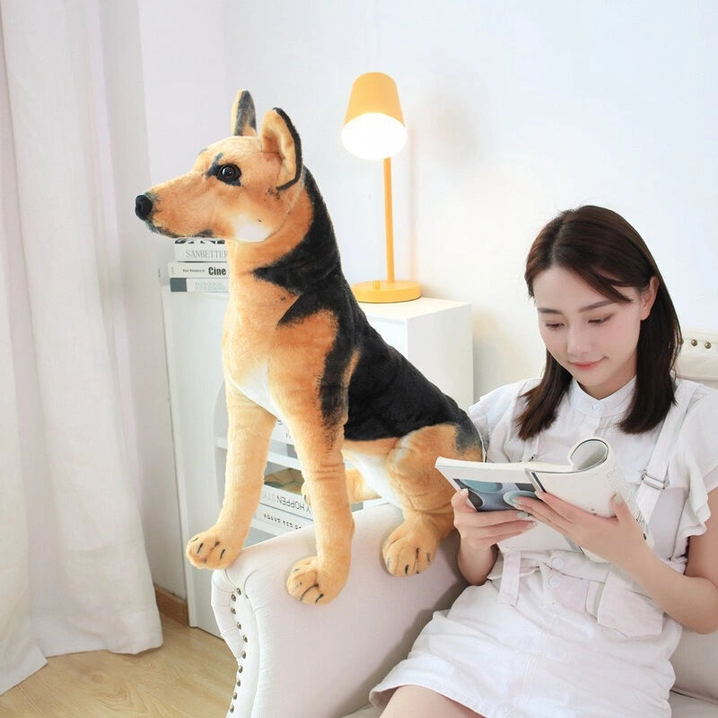 A woman reads a book on a white chair beside the ZoDoll German Shepherd Plush Realistic Stuffed Dog Toy (30cm-90cm) in a well-lit room.