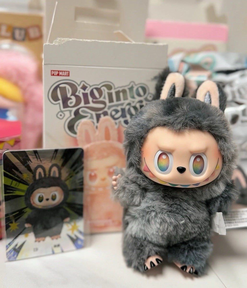 A POP MART Labubu “Secret Edition” Plush Keychain – The Monsters “Big Into Energy” Series Gray Bunny Bag Charm with rainbow eyes is displayed in front of its box and collectible card.