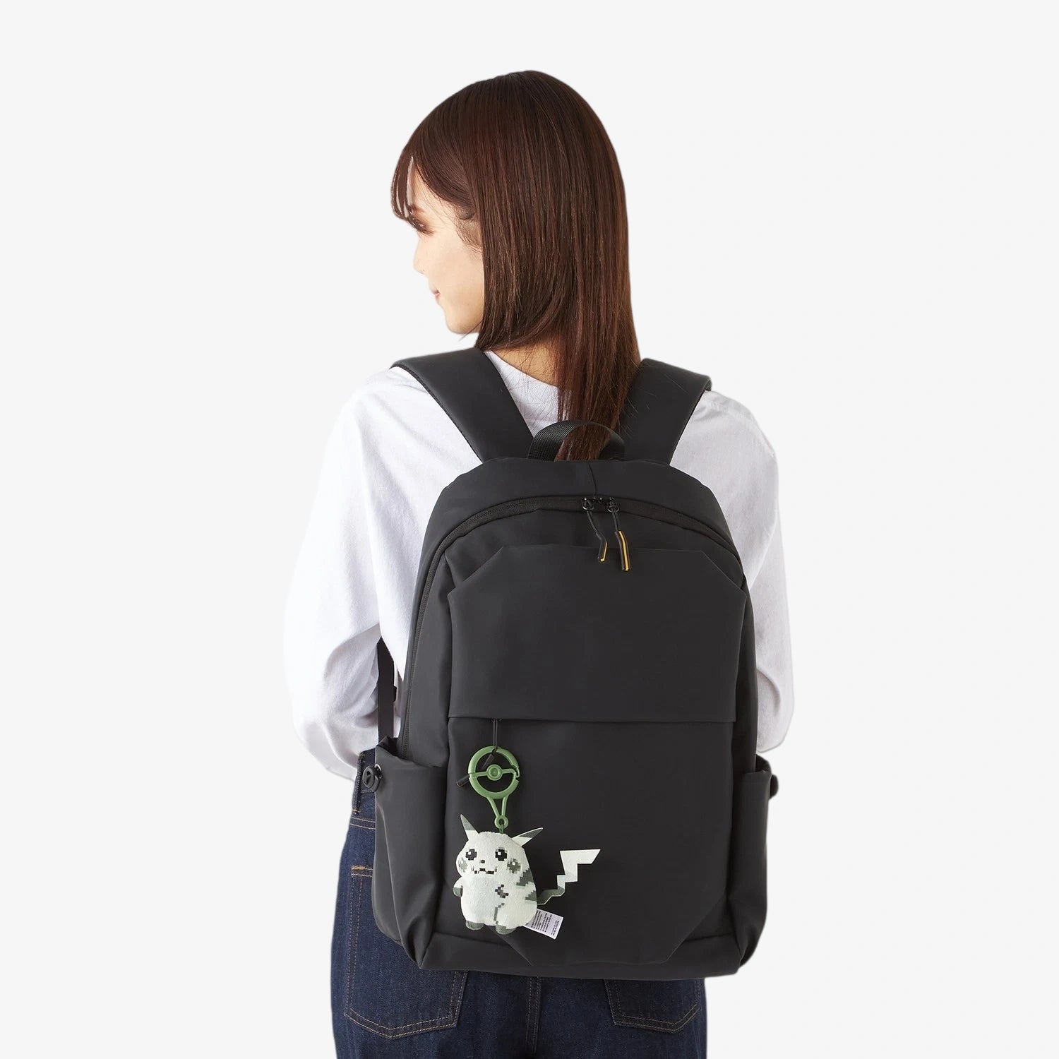 A person with straight brown hair wears a white shirt and blue overalls, carrying a ZoDoll Retro 8-Bit Pikachu of Beginnings Plush Bag Clip—Classic Chunky Pokémon 30th Anniversary keychain (12cm).