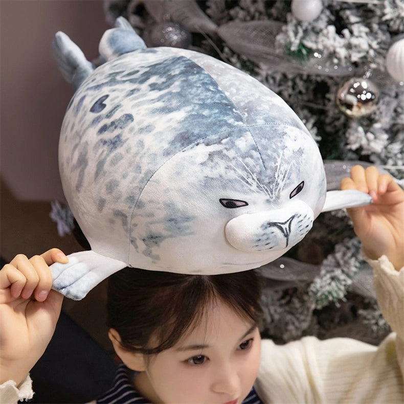 A person balances a ZoDoll Seal Plush Toys Cute Chubby Seal Plush Pillow Soft Stuffed Seal Animal (20cm/40cm) on their head in front of a Christmas tree, adding extra cheer with this adorable plush.