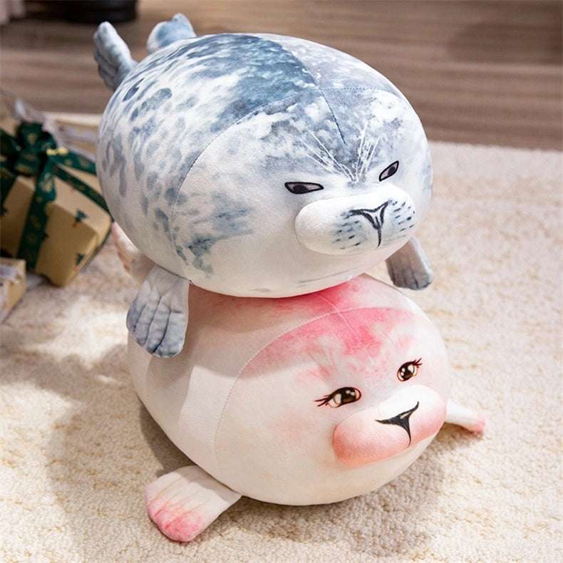 Two ZoDoll Seal Plush Toys, one gray speckled and one pinkish-white, are stacked on a carpeted floor. These cute, chubby seal plush pillows (20cm/40cm) make the perfect addition to any adorable animal plush collection.