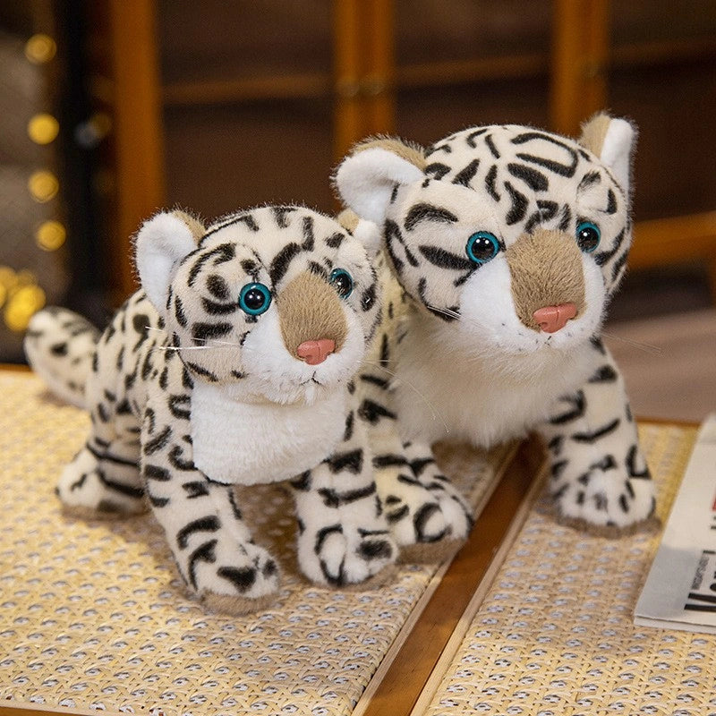 Two ZoDoll Snow Leopard Plush toys, each 43cm or 52cm, with black and white stripes and blue eyes, sit side by side indoors, capturing the charm of these realistic stuffed wild cat plushies.