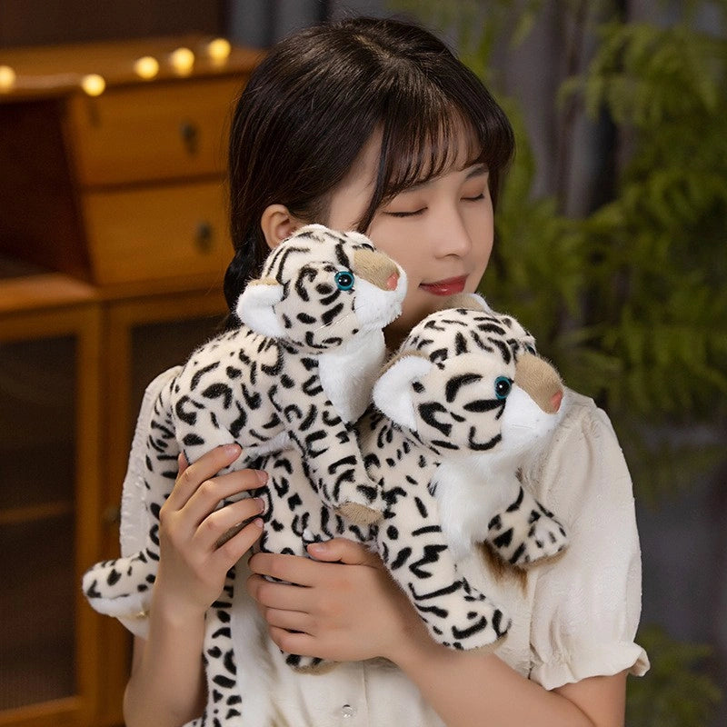 A woman with closed eyes holds two ZoDoll Snow Leopard Plush Realistic Stuffed Wild Cat Toys (43cm & 52cm), standing indoors with a wooden cabinet and a green plant in the background.