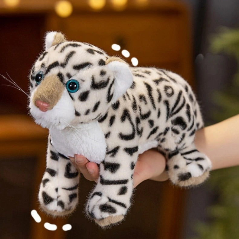A hand holds the ZoDoll Snow Leopard Plush, a realistic stuffed wild cat toy (43cm/52cm) with black spots, blue eyes, and a pink nose.