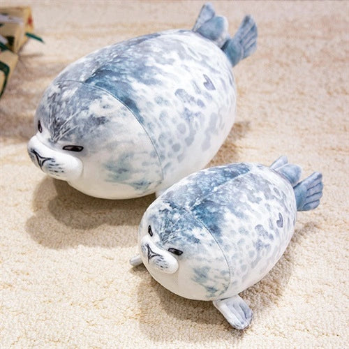 Two ZoDoll Seal Plush Toys, a 20cm and a 40cm chubby pillow with gray and white spots, sit on a beige carpet. Both have slightly grumpy faces and are perfect for cuddling or room decor.