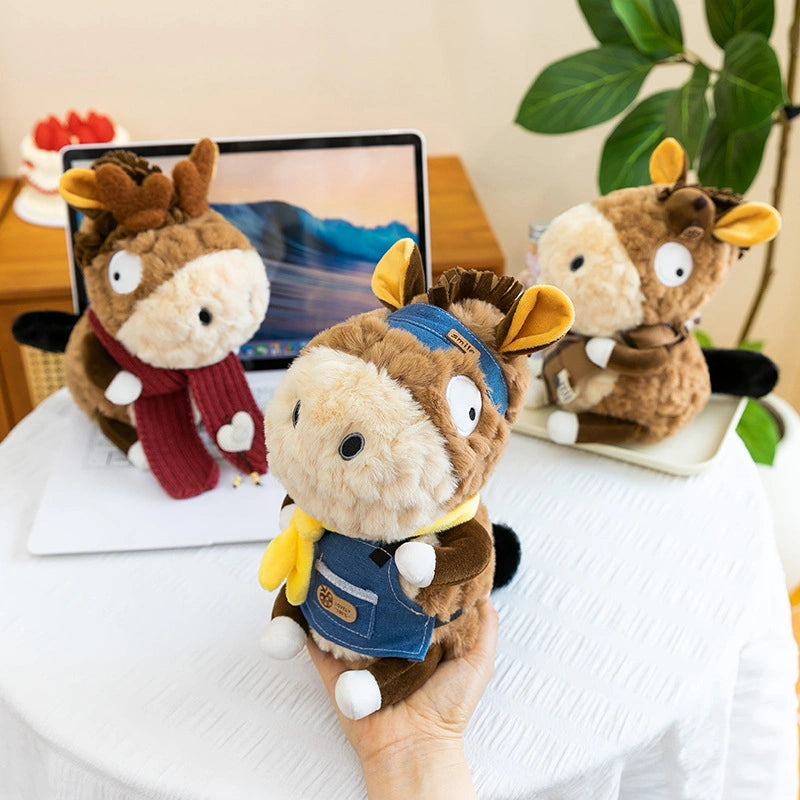 Three ZoDoll Donkey Plush Toys (23cm) with removable clothes are displayed on a table and in front of a laptop, with a plant and cake in the background.