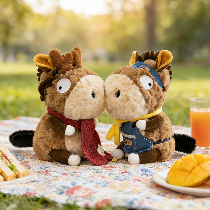Two ZoDoll Donkey Plush Toys (23cm), each with removable clothes, relax on a picnic blanket outdoors—one in a red scarf and the other in blue overalls with a yellow scarf—alongside food and juice for the perfect plush companion outing.