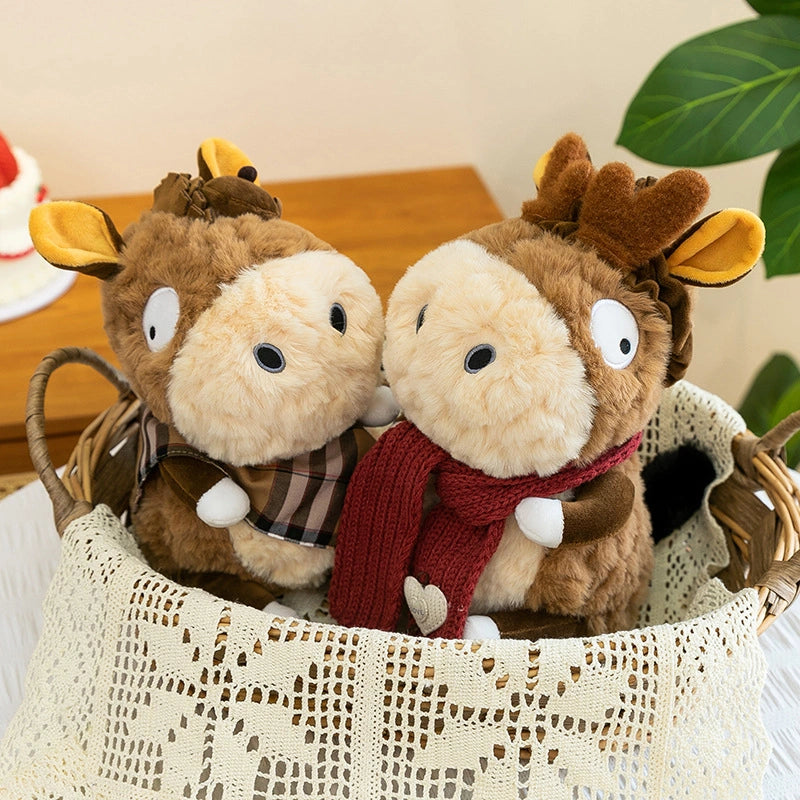 Three ZoDoll Donkey Plush Toys with big eyes and removable clothes sit in a lace-lined basket—one wearing a plaid scarf, another a red one—with a plant and cake behind them. Ideal cute plush companions for cozy scenes.