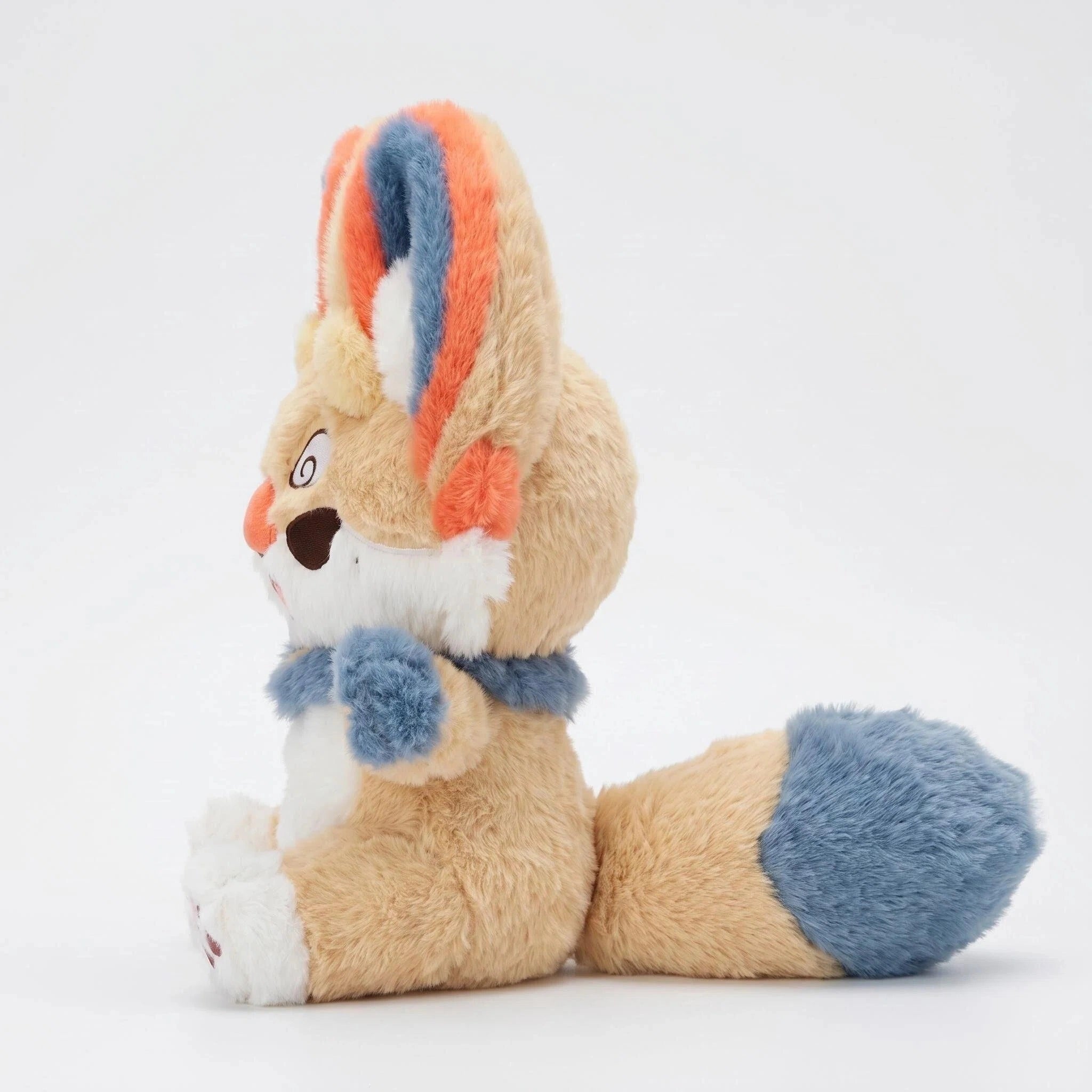 Side view of the ZoDoll Fennec Fox Plush Toy, a cute fox plush doll with big ears, tan fur, orange and blue accents, white face, blue tail tip, and blue scarf, sitting upright against a plain white background.